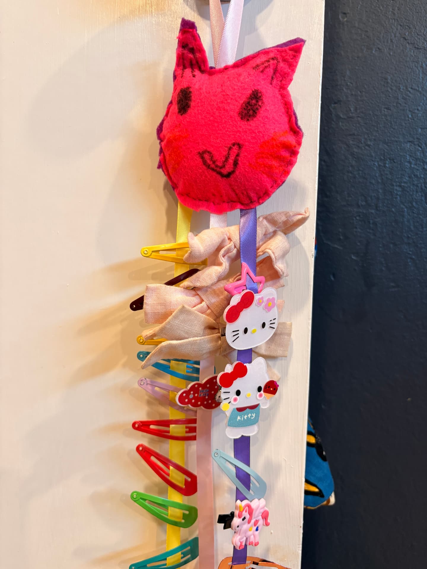 A handmade pink felt cat hair clip holder hanging on a wall with ribbons full of clips