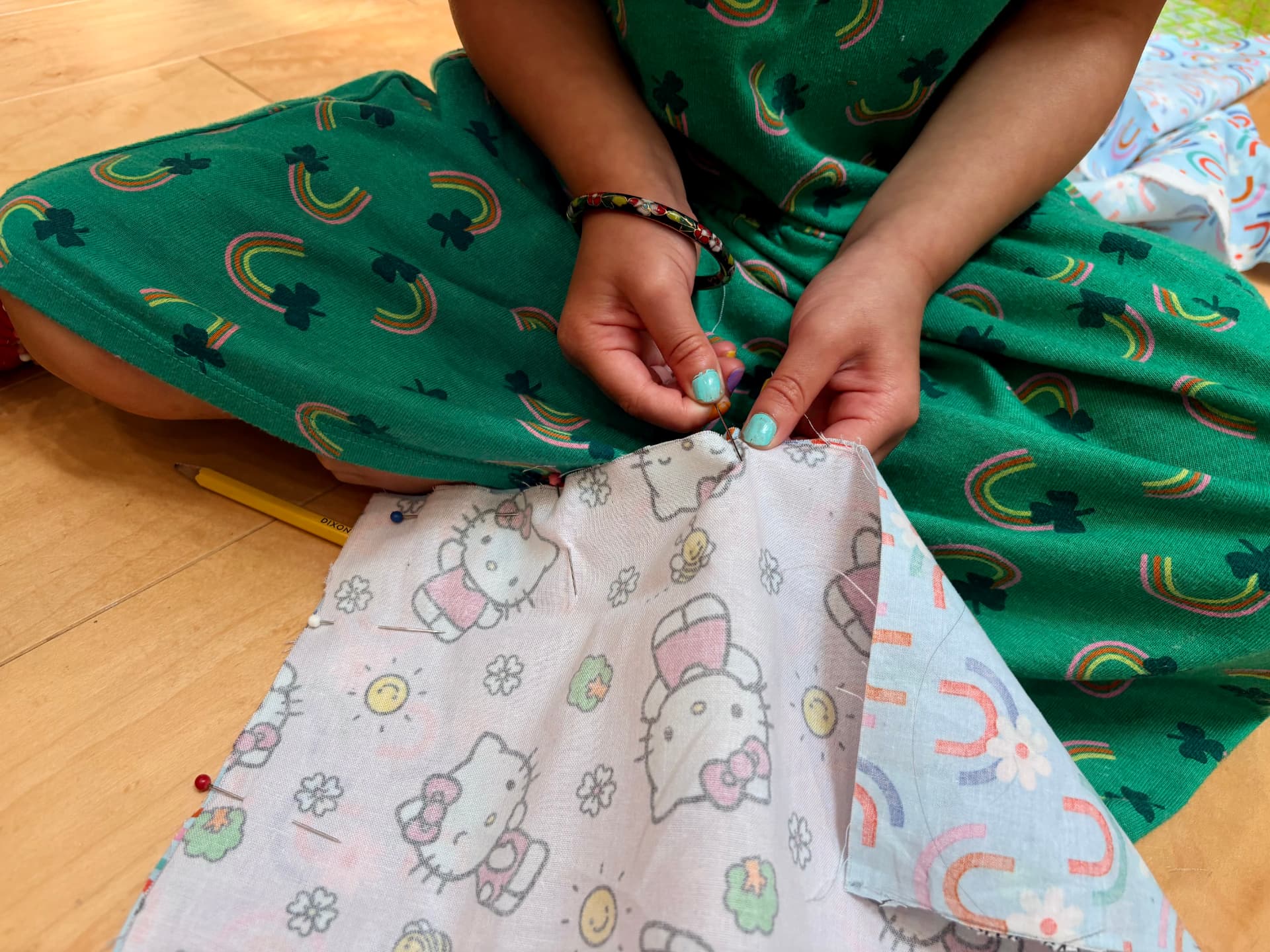 A child hand sewing a pinned Hello Kitty print fabric project while sitting on the floor