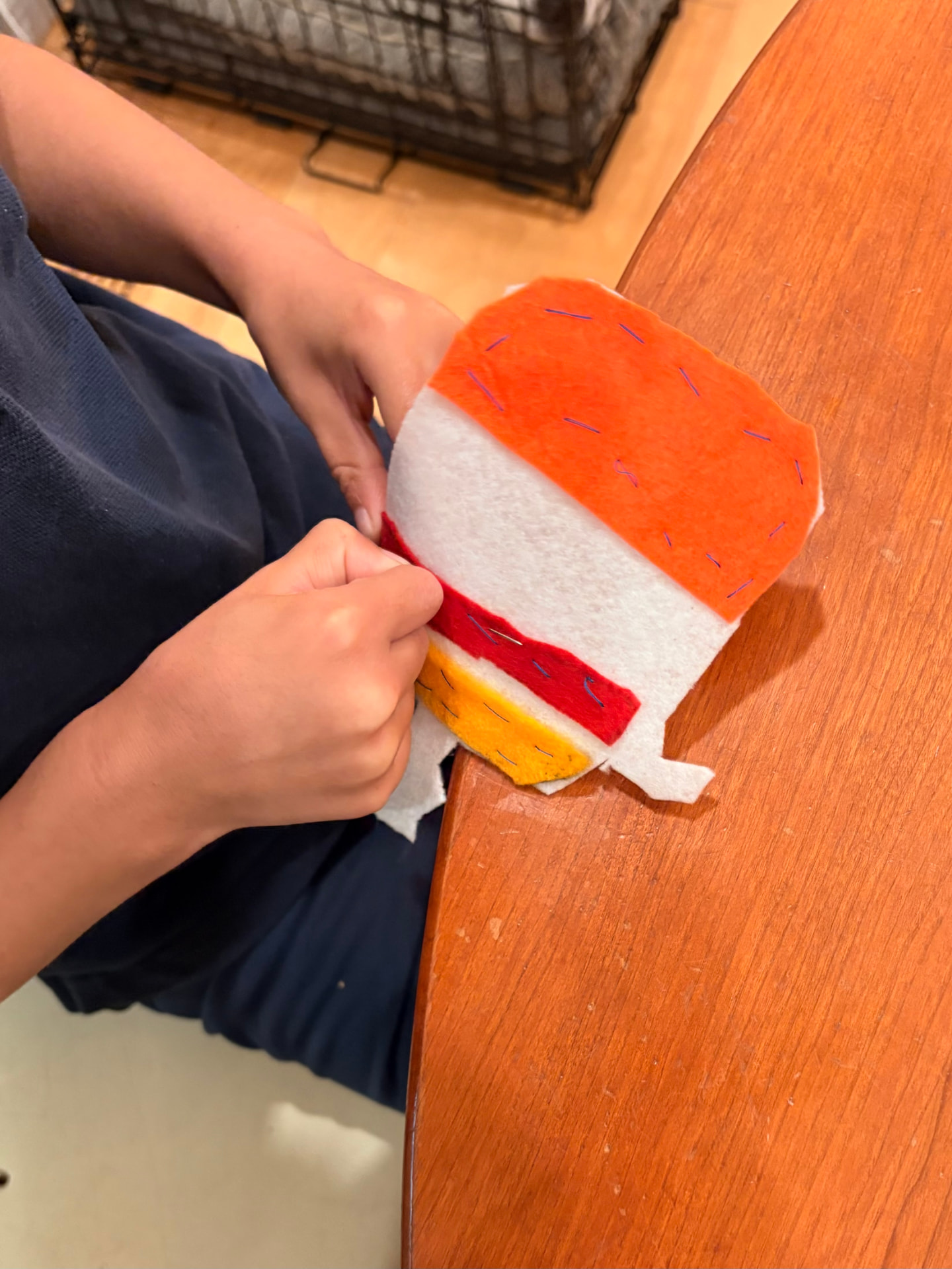 A child hand-stitching layers of orange, white, red, and yellow felt together