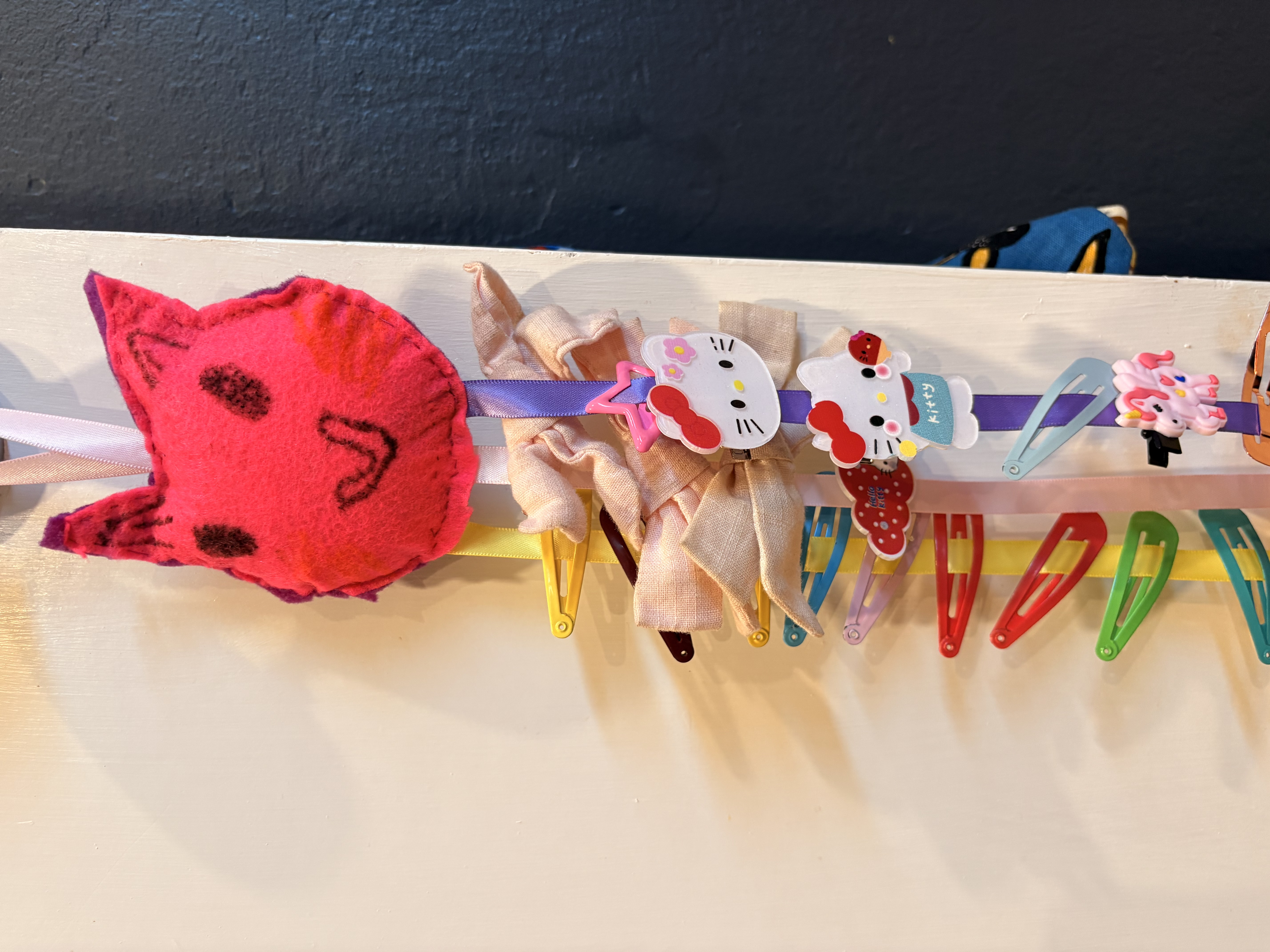 Small, round pink felt stuffed cat head with ribbons hanging to hold hair clips